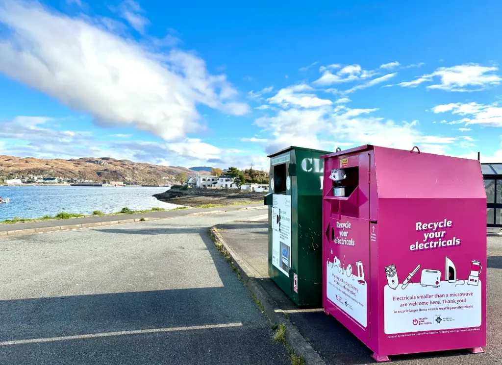 A large pink electicals collection bank in the foreground with the sea and blue sky in the background