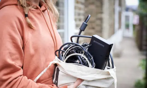 light skinned person holding a bag of electricals ready for recycling.