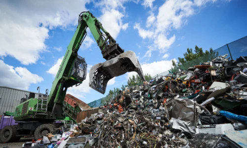 green digger outside in a recycling centre with open grabber about to pick up electricals from a mound of electrical items