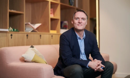 a mid shot of Material Focus CEO scott Butler sitting on a pale pink sofa