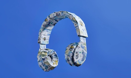 a pair of headphones that has been papier mached with British currency all over on a blue plain background
