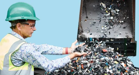 Photo shows a pale skinned male lifting a handful of metal chips that have been recycled, cutout on blue background