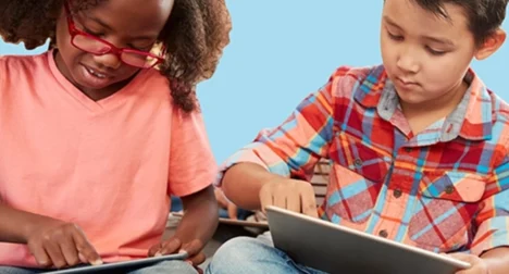 Photo shows two children, one pale skinned and one dark skinned playing on computer tablets, cutout on blue background