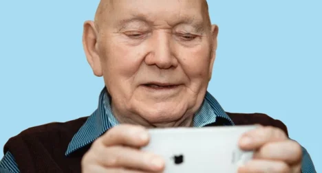 Photo shows older man looking at a moble phone, cutout on blue background