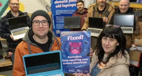 six pale skinned people of different ages holding up old laptops for recycling